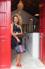 Smiling stylish black young woman with curly hair and handbag standing near red door of building — Stock Photo
