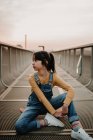 Girl sitting on skateboard on metal bridge and looking away — Stock Photo