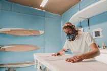 Людина в респіраторі вимірює дошку для серфінгу в майстерні — стокове фото