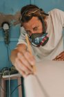 Man in respirator measuring surf board in workshop — Stock Photo
