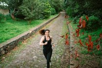 Счастливая женщина в спортивной одежде бегает по дорожке в парке — стоковое фото