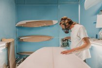 Mann mit Werkzeug sägt Surfbrett in Werkstatt — Stockfoto
