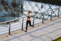 Сверху женщины в спортивной одежде бегают по набережной возле воды в городе — стоковое фото