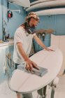Hombre en respirador puliendo tabla de surf en taller - foto de stock