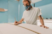 Homme en respirateur mesurant la planche de surf en atelier — Photo de stock