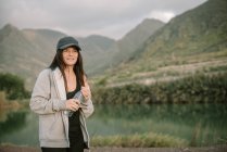 Frau in Sportbekleidung trinkt Wasser am See zwischen Bergen — Stockfoto