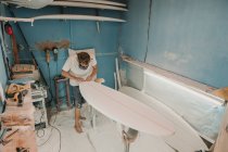 Hombre en respirador puliendo tabla de surf en taller - foto de stock