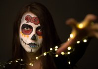 Giovane donna con vernice viso raccapricciante che tiene luci fata — Foto stock