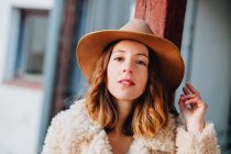 Positive attraktive junge Frau in warmer Kleidung und Hut blickt in die Kamera — Stockfoto