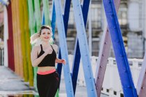 Donna in abbigliamento sportivo con auricolari e smartphone in esecuzione su strada — Foto stock