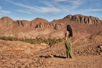 Rückansicht einer jungen brünetten Dame, die zwischen Wüstenland in der Nähe von antiken Bauten und Hügeln in Marrakesch, Marokko, steht — Stockfoto