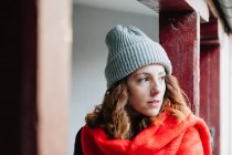 Дружня молода жінка в зимовому одязі дивиться вниз і стоїть біля будівлі — стокове фото