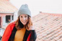 Friendly young woman in winter looking at camera and standing near building — Stock Photo