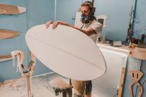 Homme tenant une planche de surf sur le stand en atelier — Photo de stock