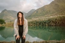 Mulher positiva ter uma pausa depois de correr na natureza perto do lago e montanhas — Fotografia de Stock