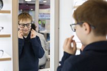 Carino giovane ragazzo cercando su occhiali in un negozio di occhiali — Foto stock