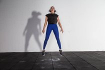 Atletica giovane signora concentrata in abbigliamento sportivo facendo squat e saltando in palestra — Foto stock