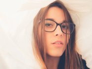 Teenager mit Brille blickt zwischen weißem Material auf Kamera — Stockfoto
