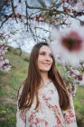Ramoscelli di albero da frutto in fiore e sorridente giovane donna che guarda lontano nella natura — Foto stock