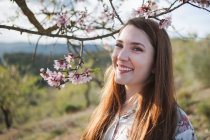 Zweige blühender Obstbäume und glückliche junge Frau, die in der Natur wegschaut — Stockfoto