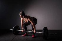 Vue latérale de la jeune femme concentrée athlétique en tenue de sport haussant la barre au-dessus de la tête dans la salle de gym — Photo de stock