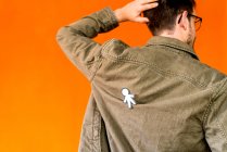 Вид сзади парня с бумажным силуэтом на апрельский день дураков на джинсовой куртке на оранжевом фоне — стоковое фото