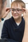 Carino giovane ragazzo cercando su occhiali in un negozio di occhiali — Foto stock