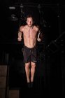 Sportlicher junger Mann ohne Hemd hängt in Turnhalle an Turnringen zwischen Dunkelheit — Stockfoto