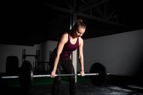 Athletische junge konzentrierte Dame in Sportbekleidung, die im Fitnessstudio die Langhantel über den Kopf zieht — Stockfoto