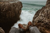 Jambes de culture de l'homme assis sur le dessus de la pierre près de la mer orageuse dans bufones de pria, asturias, espagne — Photo de stock