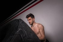 Atlético jovem shirtless cara ter competição de lançando grandes pneus no ginásio — Fotografia de Stock