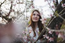 Zweige blühender Obstbäume und sinnliche junge Frau, die in der Natur wegschaut — Stockfoto