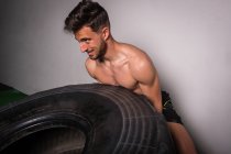 Спортивний молодий без сорочки хлопець змагається з перекидання великих шин у спортзалі — стокове фото