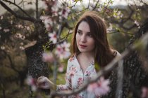 Веточка цветущего фруктового дерева и заботливая молодая женщина, смотрящая вдаль на природу — стоковое фото