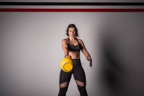 Atlética joven mujer concentrada en ropa deportiva subiendo kettlebell en el gimnasio - foto de stock