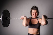 Athletic young concentrated lady in sportswear upping barbell above head in gym — Stock Photo
