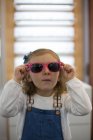 Jeune fille mignonne essayant des lunettes dans un magasin de lunettes — Photo de stock
