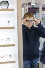 Lindo chico joven probándose gafas en una tienda de gafas - foto de stock
