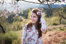 Twigs of blooming fruit tree and cheerful young woman looking away in nature — Stock Photo