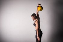 Athlète jeune femme concentrée dans les vêtements de sport kettlebell upping dans la salle de gym — Photo de stock