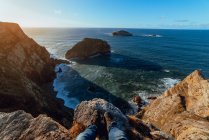 Crop legs of human sitting on top of stone hill near pitoresco sea in sunny day in Cabo de Penas, Astúrias, Espanha — Fotografia de Stock