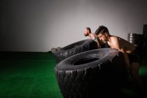 Side view of athletic young shirtless guys having competition of flipping big tires in gym — Stock Photo
