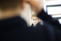 Милий молодий хлопчик приміряє окуляри в магазині одягу — стокове фото