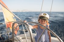 Positives Kind mit Kapitänsmütze schwimmt bei sonnigem Tag auf teurem Boot auf See — Stockfoto