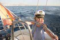 Positive kid in captain hat floating on expensive boat on sea in sunny day — Stock Photo
