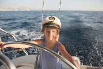 Positive kid in captain hat floating on expensive boat on sea in sunny day — Stock Photo
