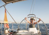 Enfant positif en chapeau de capitaine flottant sur un bateau cher sur la mer par temps ensoleillé — Photo de stock