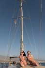 Belle giovani donne in occhiali da sole e cappelli capitano sul ponte laterale di costosa barca galleggiante sull'acqua nella giornata di sole — Foto stock
