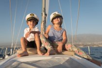 Crianças positivas em chapéus capitão sentado no convés de barco caro flutuando na água em dia ensolarado — Fotografia de Stock