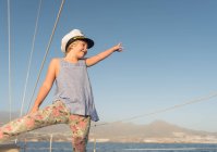 Positive girl in captain hat sitting on deck of expensive boat floating on water in sunny day — Stock Photo